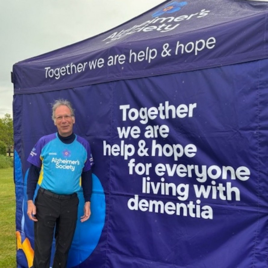 Our CEO David Gent at a Alzheimer's Society tent smiling at the camera before he embarks on a 13 mile hike for charity.
