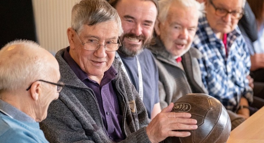 A group of man sat at a table while smiling and holding a football