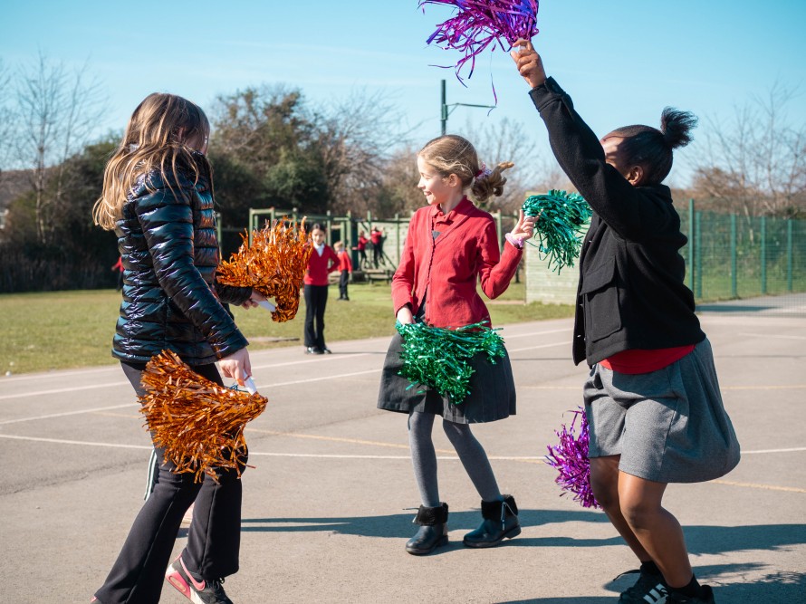 Three girls dances with pom poms in the school playground